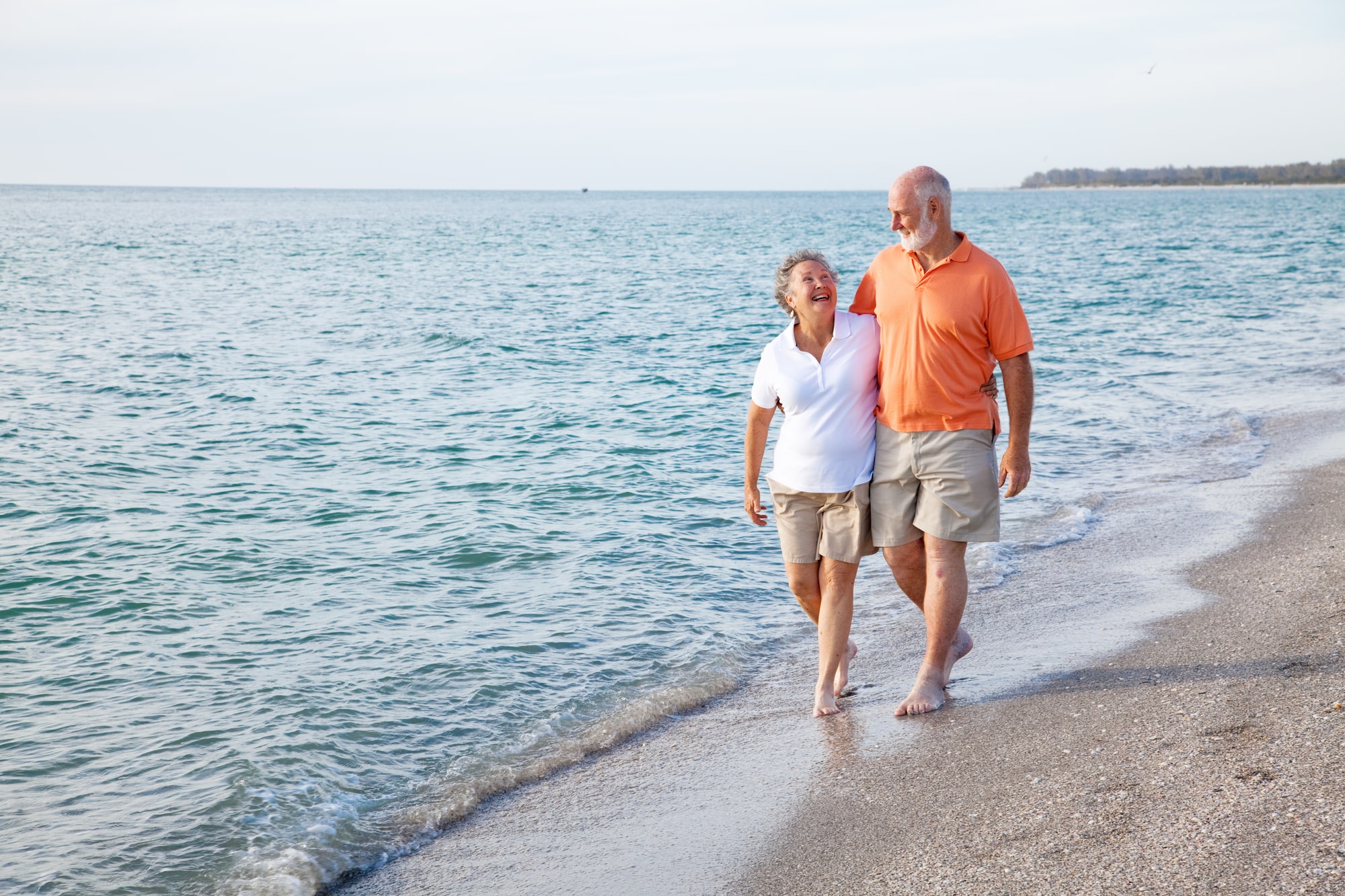 Elderly couple laughing and walking on a beach